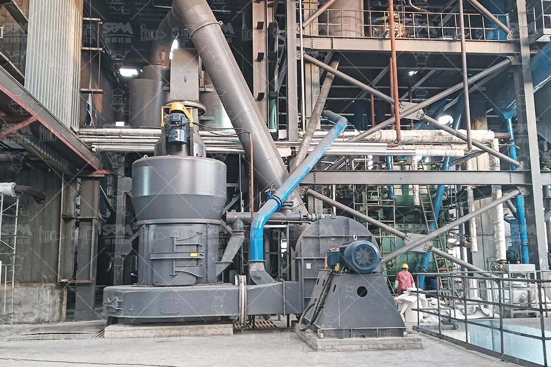Industrial grinding mill in operation within a mineral processing plant, showing material feed and control systems.